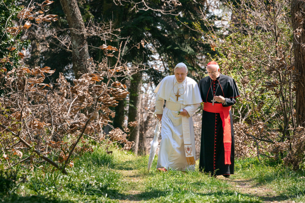 Still from the movie The Two popes showing  Anthony Hopkins as Pope Benedict XVI and Jonathan Pryce as Cardinal Jorge Mario Bergoglio walking together.